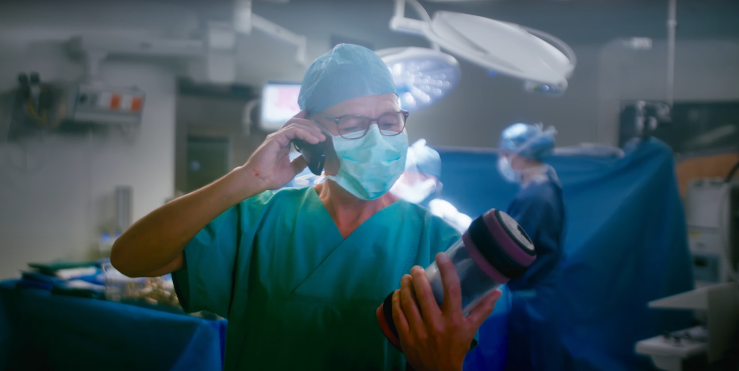 Vue de face d'une personne en salle d'opération qui tient un tube téléphonique dans la main et qui parle au téléphone.