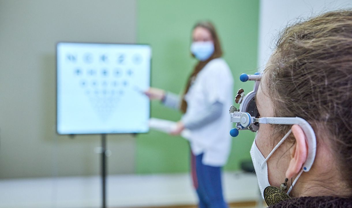 Ärztin untersucht die Sehfähigkeit einer Patientin mithilfe einer Tafel 