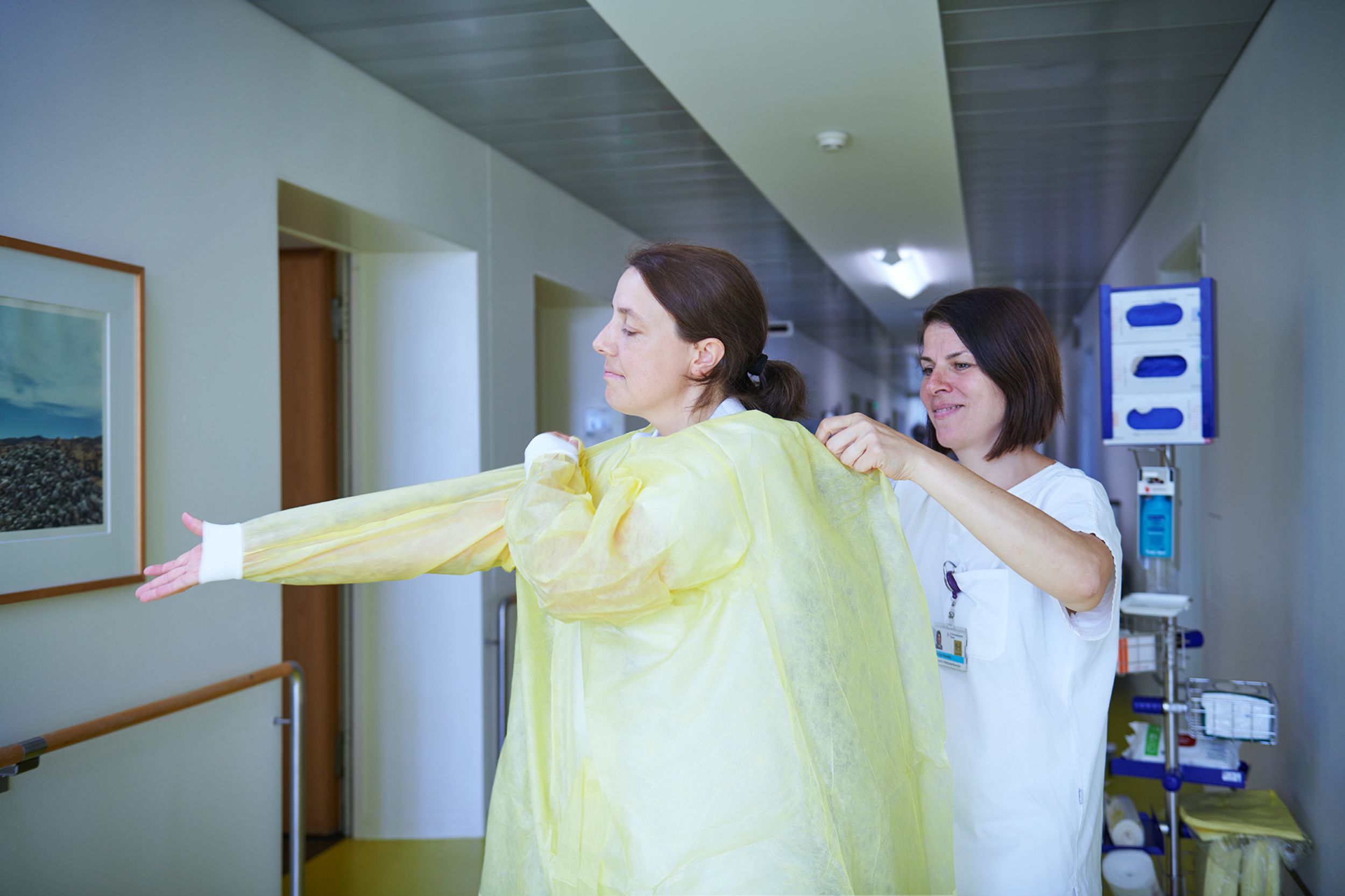Deux collaboratrices du service d'hygiène hospitalière s'aident mutuellement à enfiler des vêtements de protection
