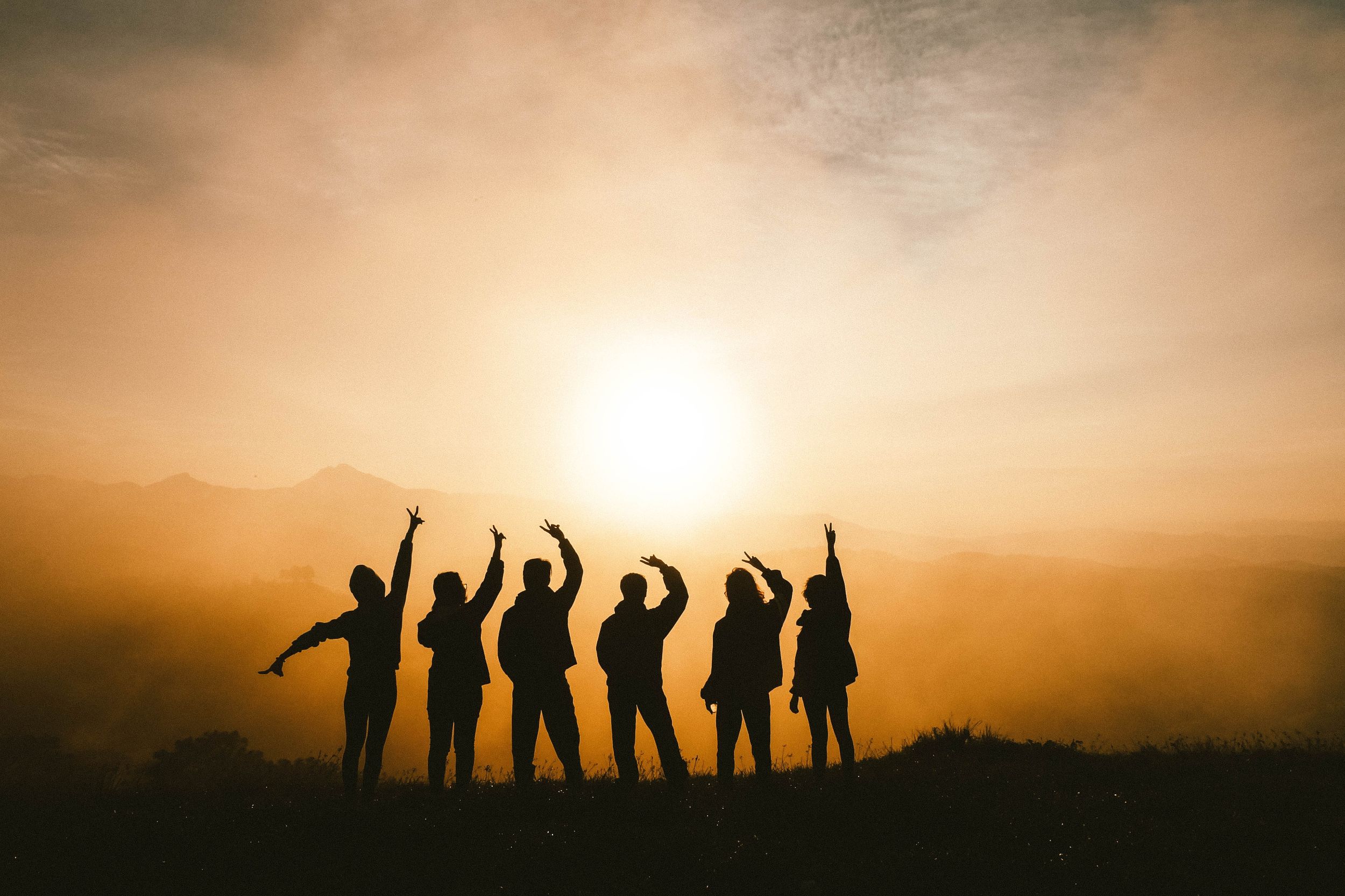 Gruppe vor Sonnenaufgang mit den Händen in der Luft 
