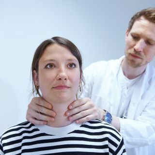 Arzt tastet Hals von Patientin ab
