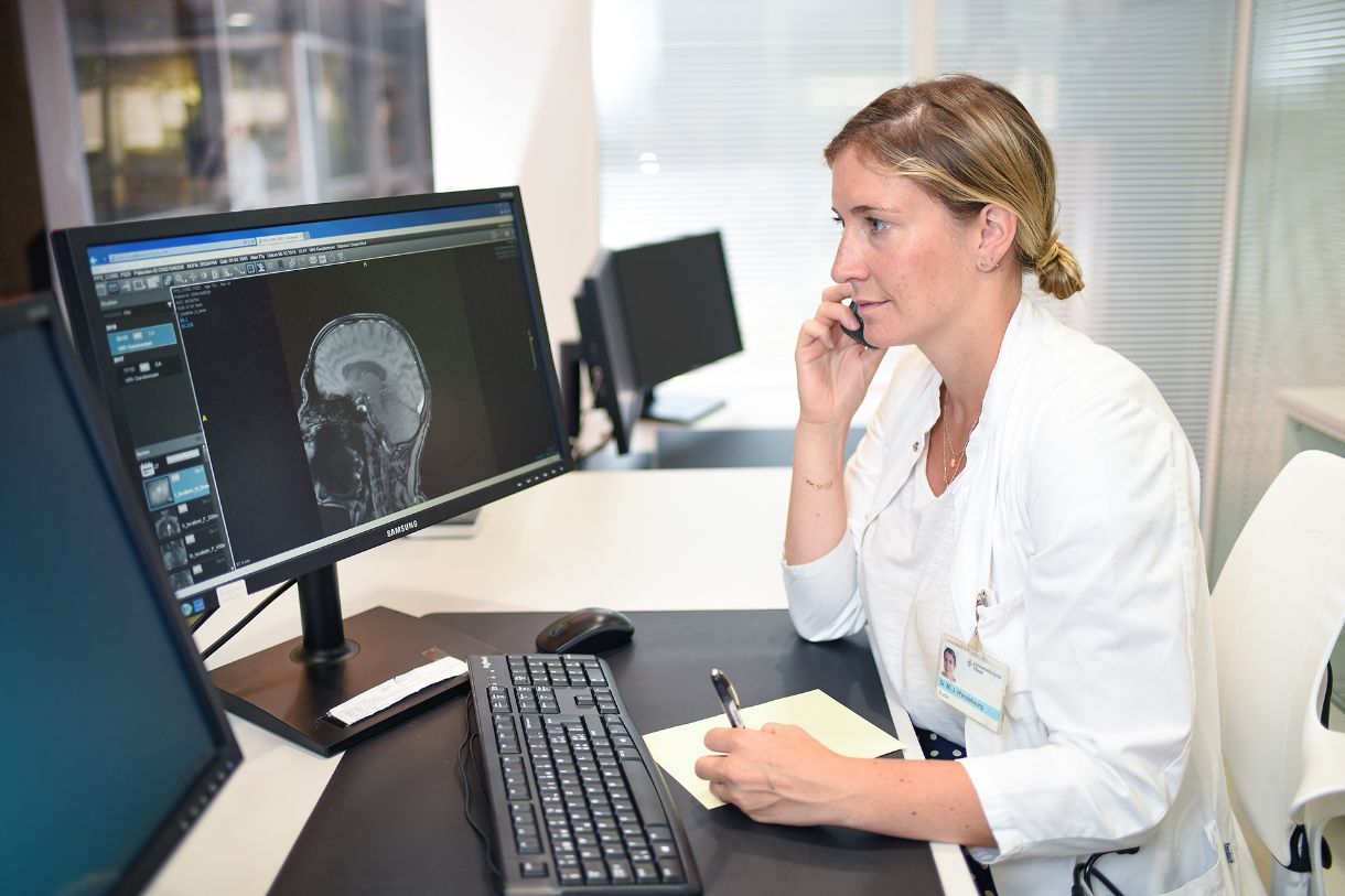 Dr. Maria Wendebourg telefoniert vor Computer mit Bild eines Gehirn-Scans