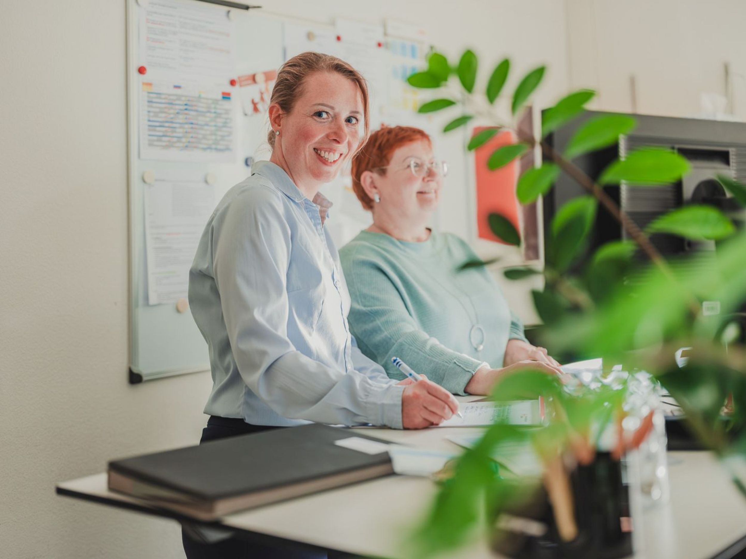 Ein lächelnder Mann sitzt an einem Tisch und arbeitet an einem Laptop, während eine Frau neben ihm sitzt und ebenfalls lächelt.