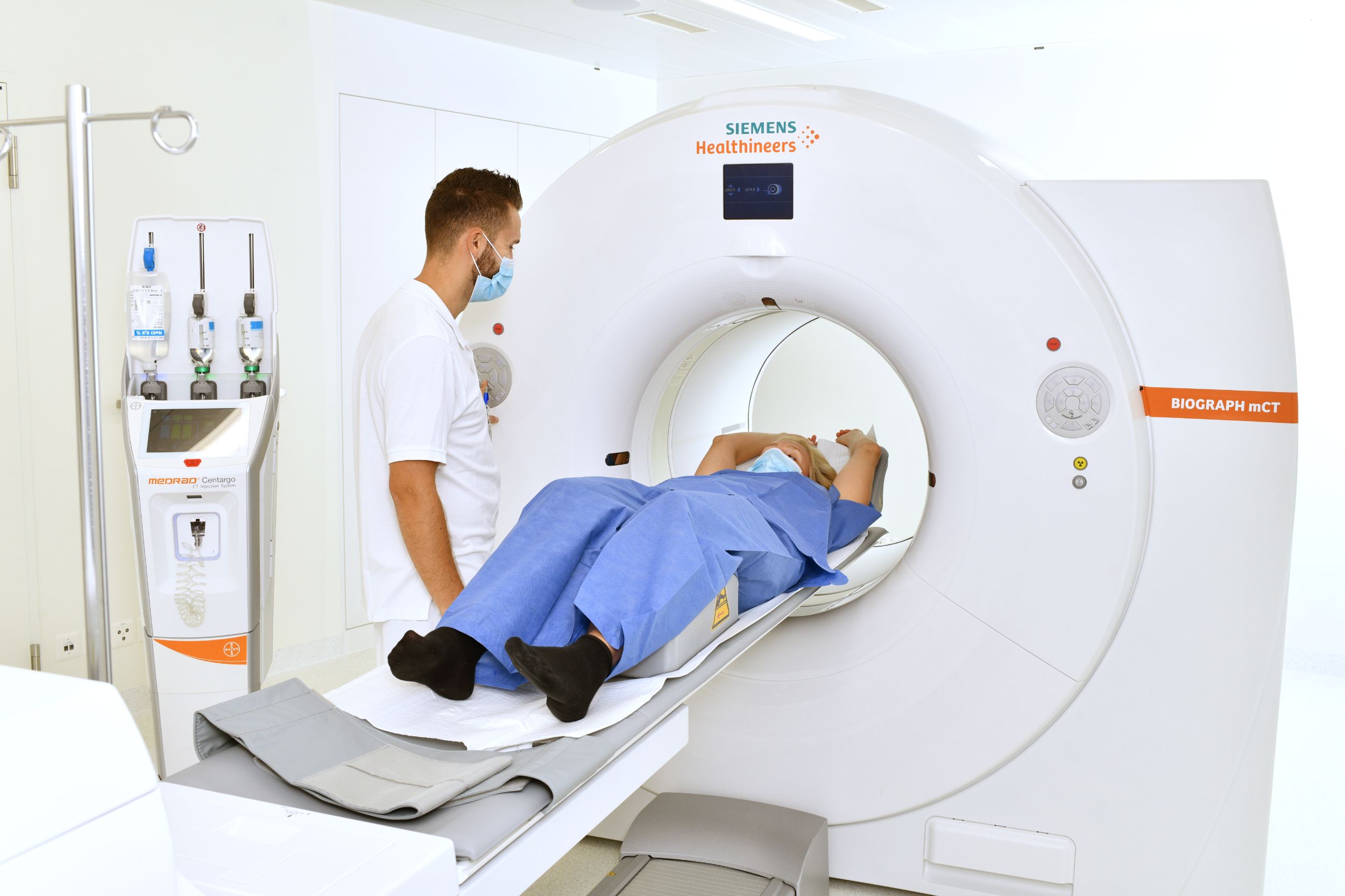 Blick von Vorne auf ein MRI Gerät, Pflegender im Gespräch mit Patientin