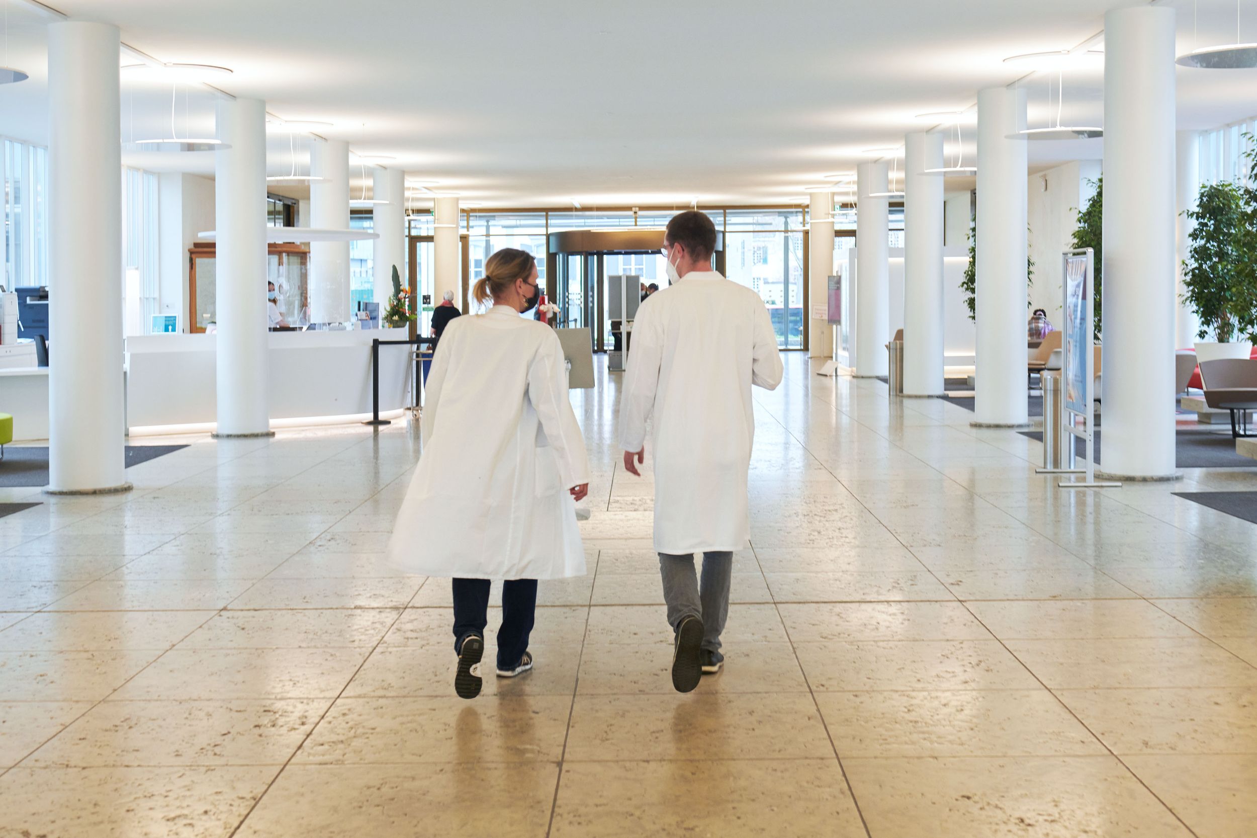 Arzt und Ärztin laufen durch Eingangsbereich K1