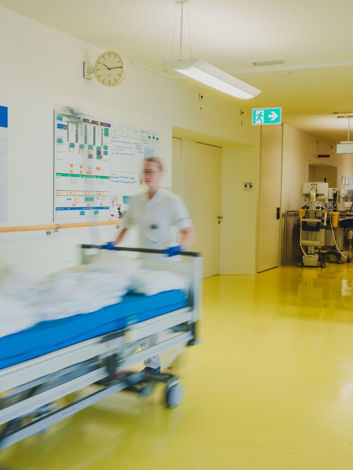 Quatre personnes, trois femmes et un homme, sont debout ou assises autour d'un écran d'ordinateur dans un environnement de travail. Les femmes portent des vêtements de travail blancs et verts, l'homme également du blanc. Ils sont concentrés sur l'écran, peut-être en train de discuter ou de vérifier quelque chose. En arrière-plan, on voit des murs avec des documents et un autre poste de travail informatique. La scène montre une activité professionnelle commune dans le domaine médical.
