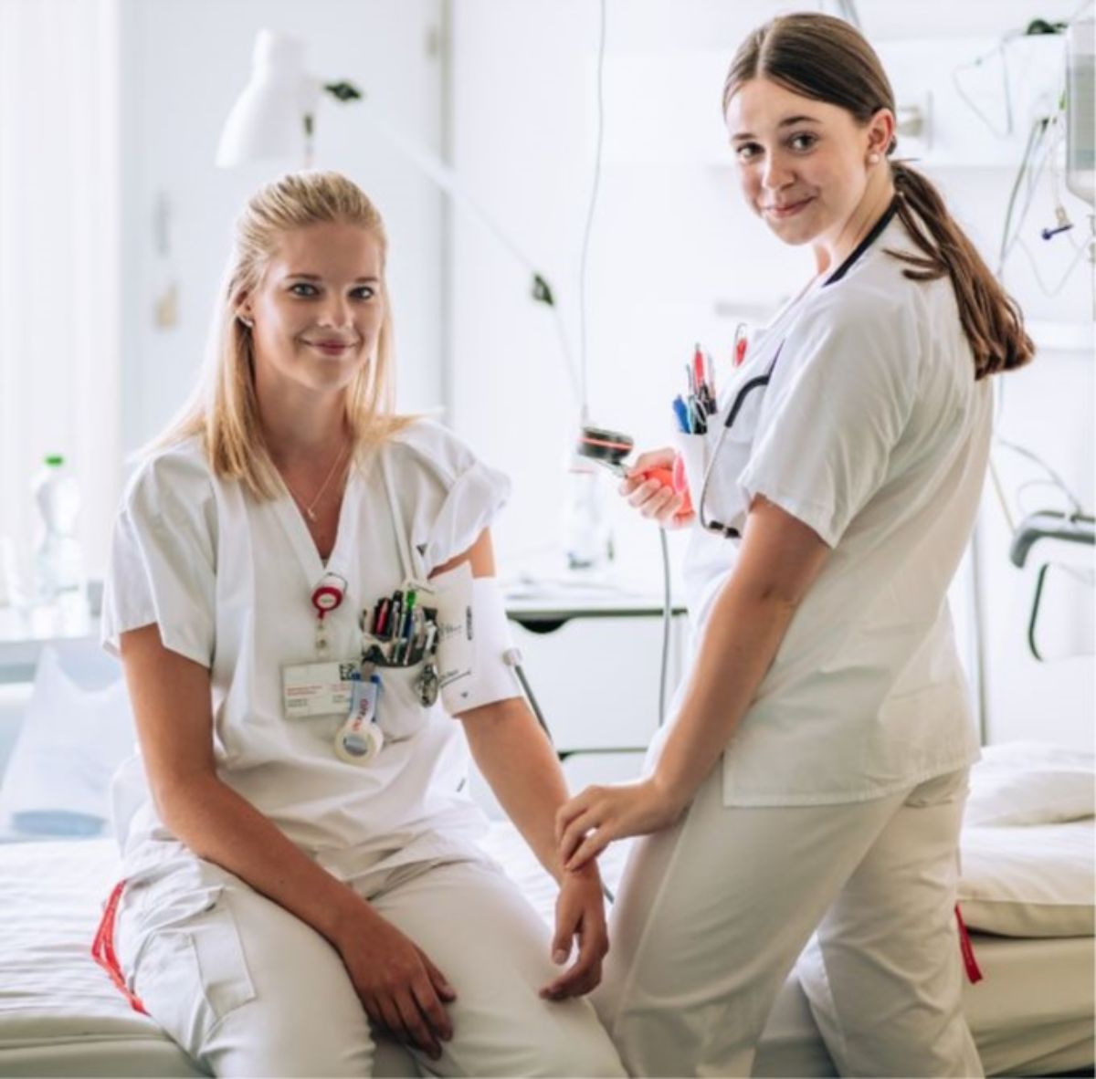 Zwei Fachfrauen Gesundheit (FaGe) in Ausbildung sitzen und stehen am Patientenbett
