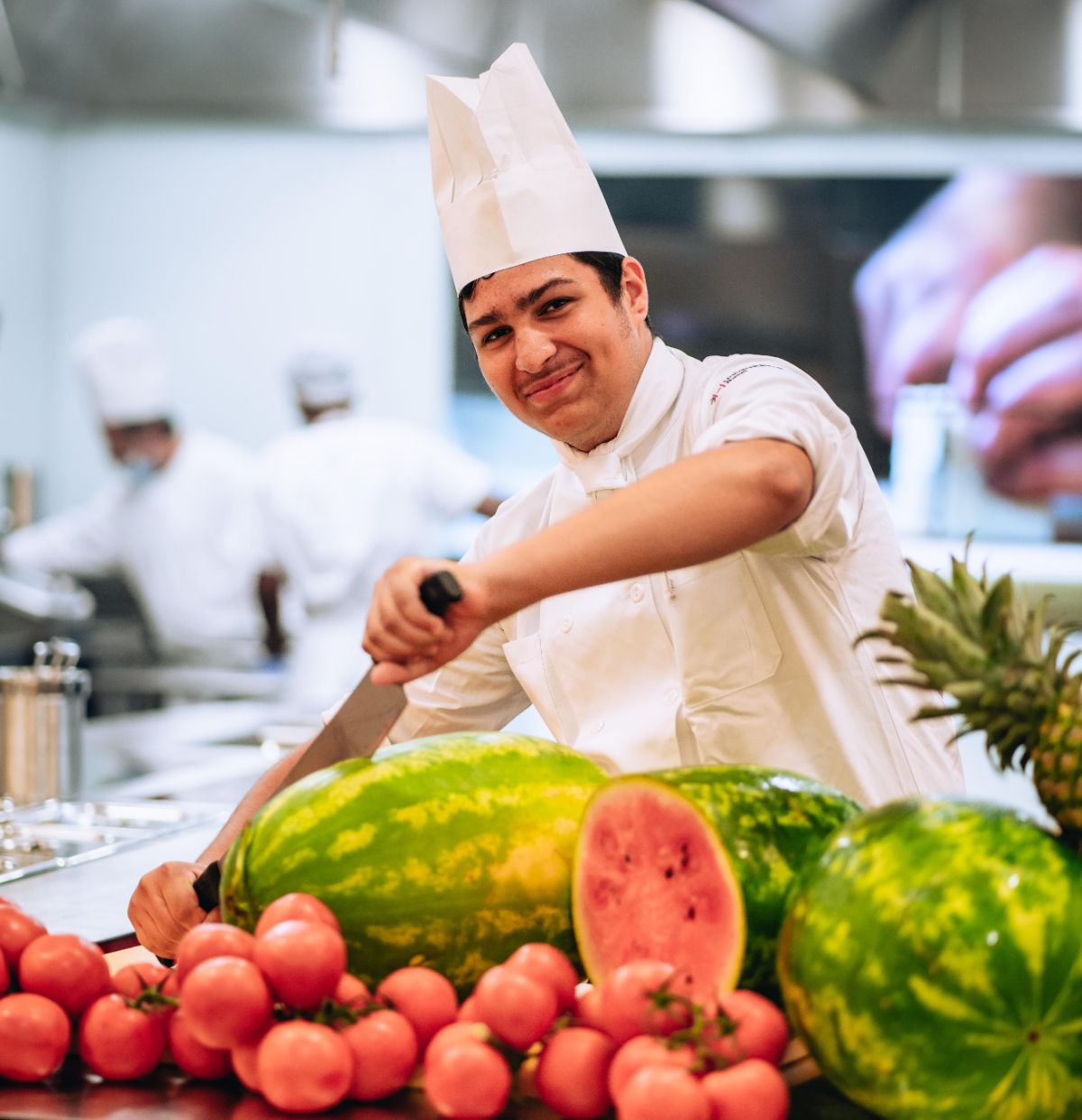 Koch in Ausbildung schneidet mit einem Messer eine grosse Wassermelone