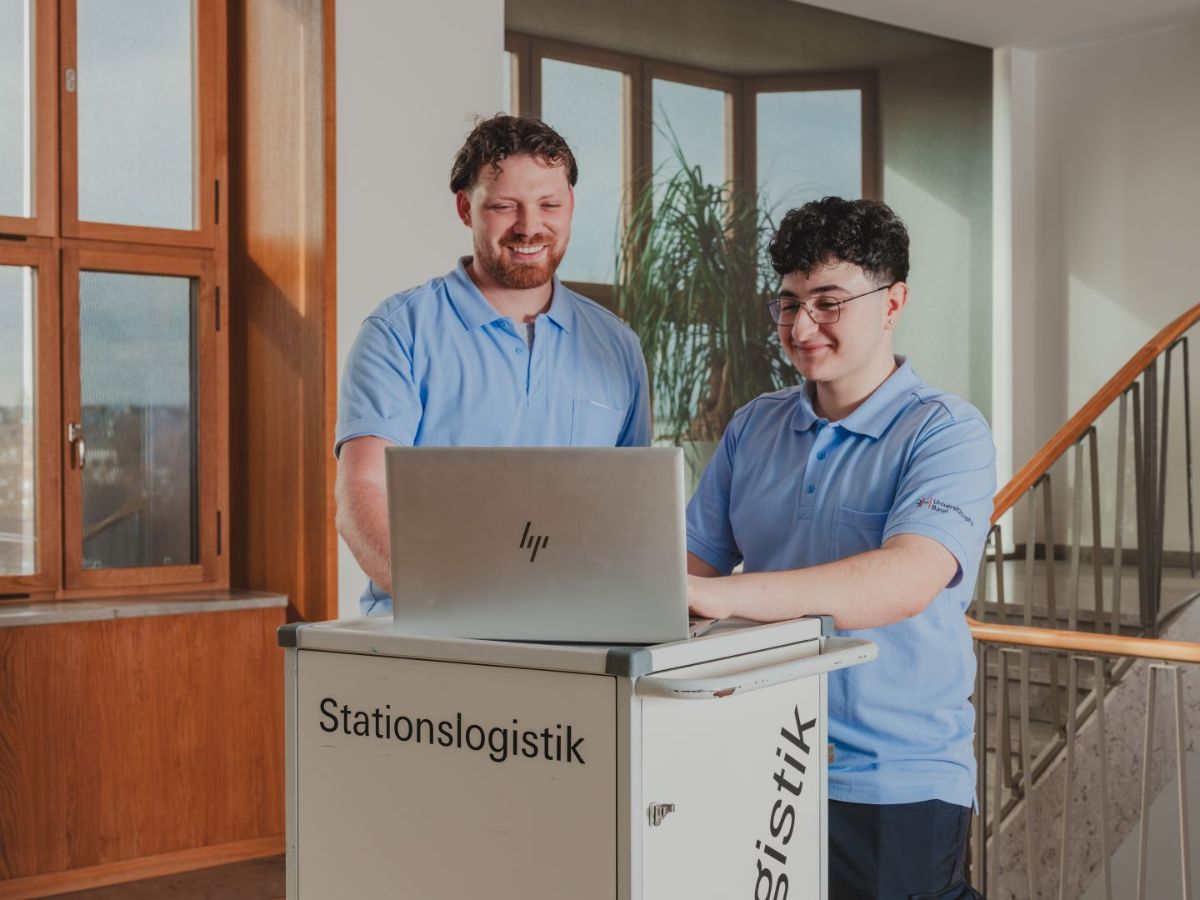 Zwei Mitarbeitende arbeiten gemeinsam an einem Laptop auf einem Wagen der Stationslogistik.