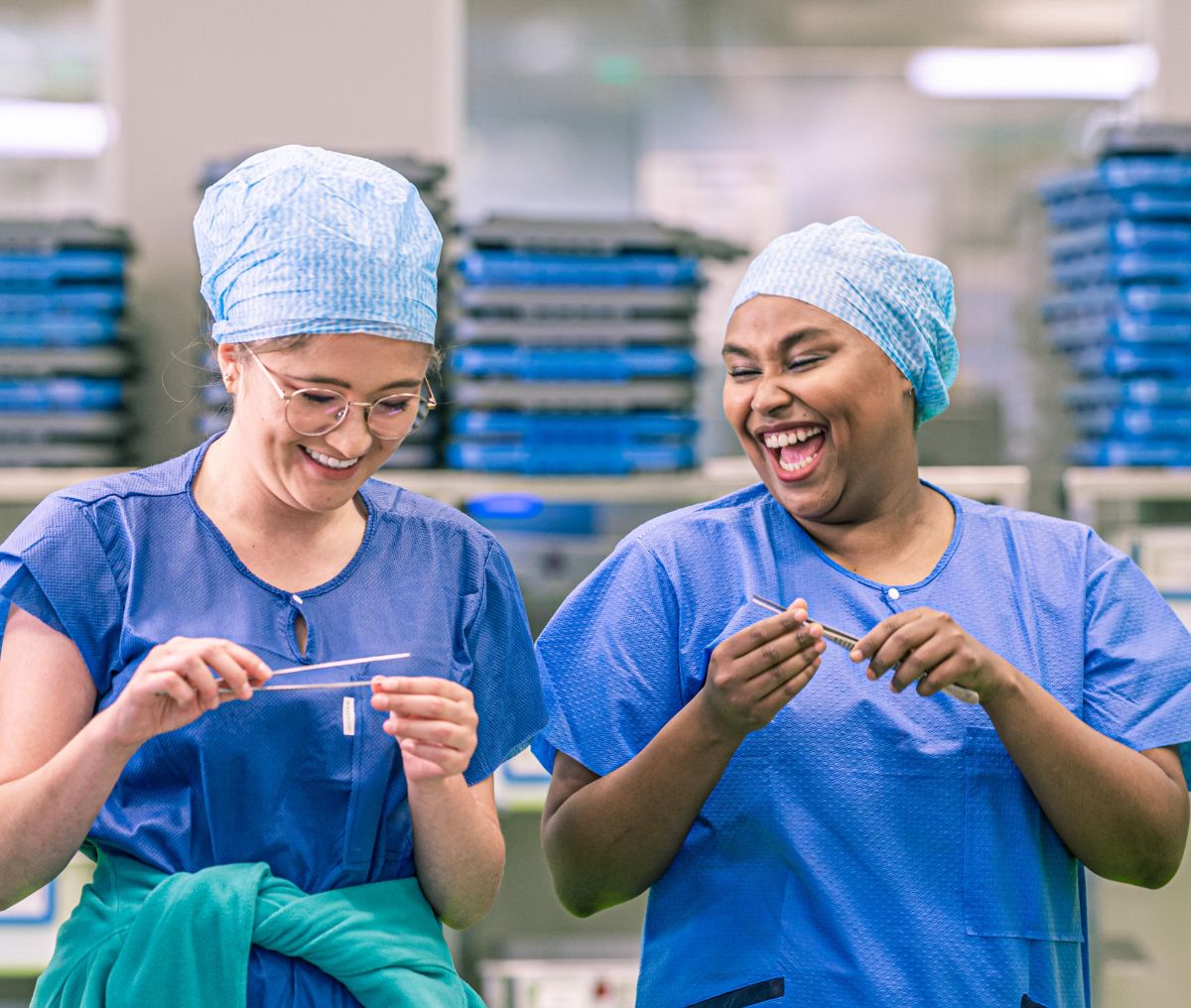 Zwei Medizinproduktetechnologinnen in Ausbildung haben medizinisches Equipment in der Hand und lachen zusammen