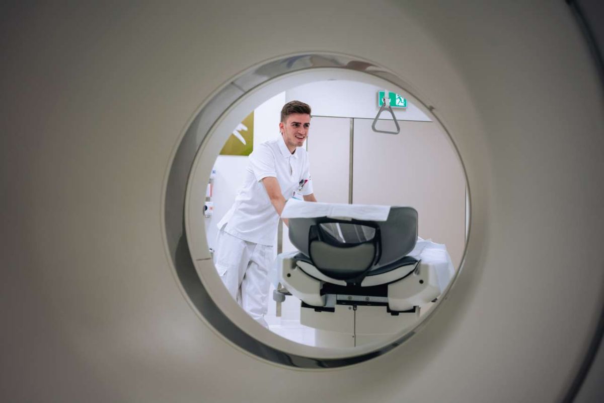 Radiologiefachmann in weisser Berufskleidung steht an einem MRT-Gerät und bereitet die Untersuchung vor.