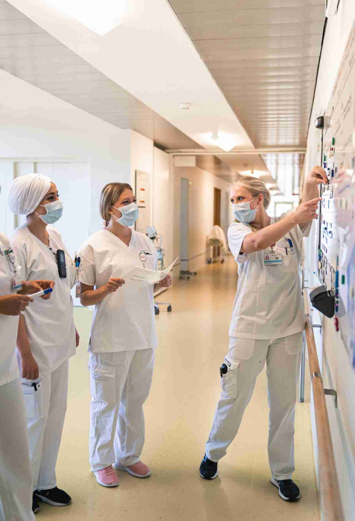 Pflegefachfrauen m weissen Kittel und mit Mundschutz besprechen sich vor einem Belegungs- oder Organisationsboard auf der Station.