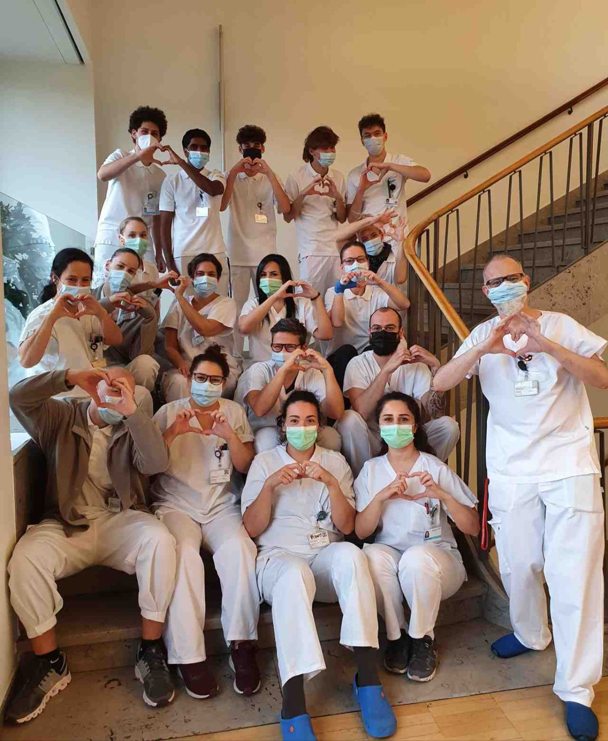A group of caregivers sits on the stairs and makes the heart gesture